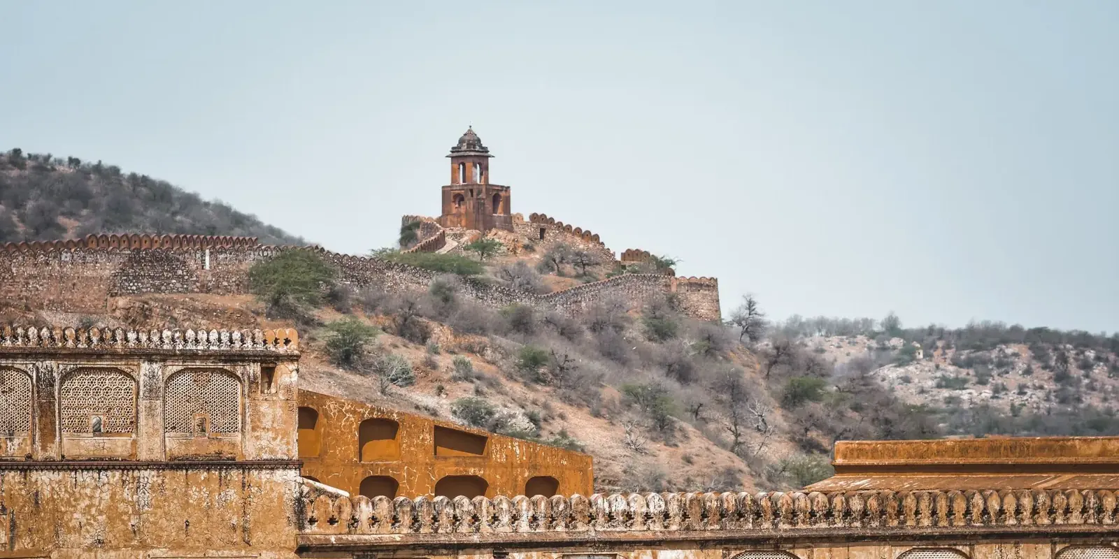 Le colline aride degli Aravalli ad Amer, con le mura e una torre di guardia sul crinale e un antico palazzo in primo piano