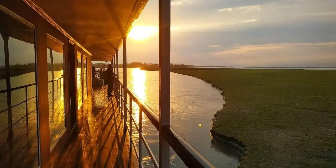 Il ponte di legno di una nave da crociera sul Brahmaputra al tramonto, con il sole riflesso sul fiume