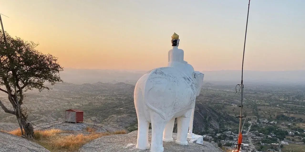 La statua bianca dell'elefante sulla cima di granito sopra Narlai, vista da dietro, con la pianura nella luce del tramonto