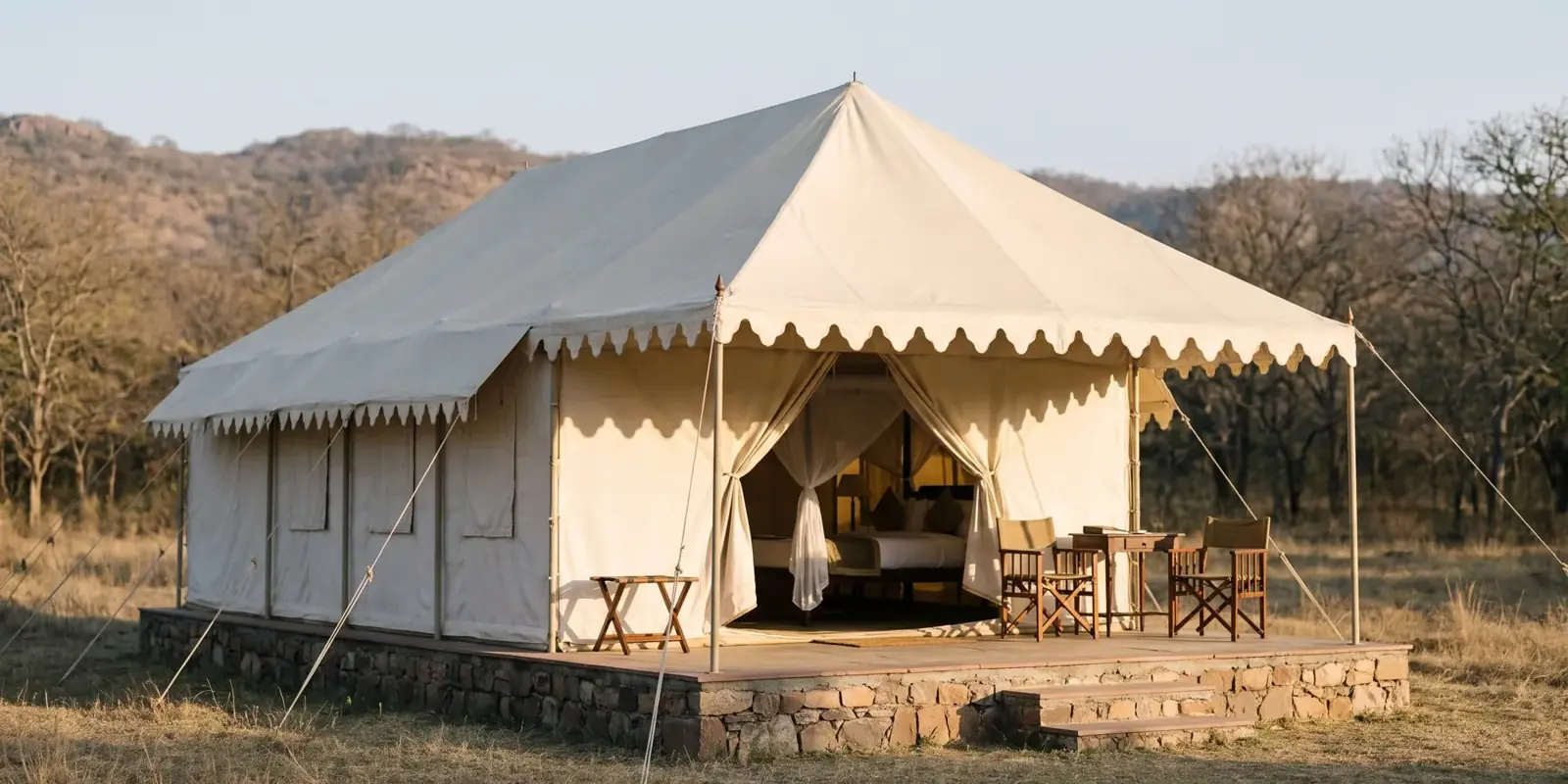 Tenda safari di tela chiara in stile anni Venti, con veranda su una base di pietra, ai margini della foresta secca di Ranthambore