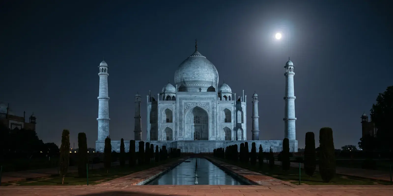 Il Taj Mahal di notte sotto la luna piena, visto da sud lungo il canale e i cipressi del giardino