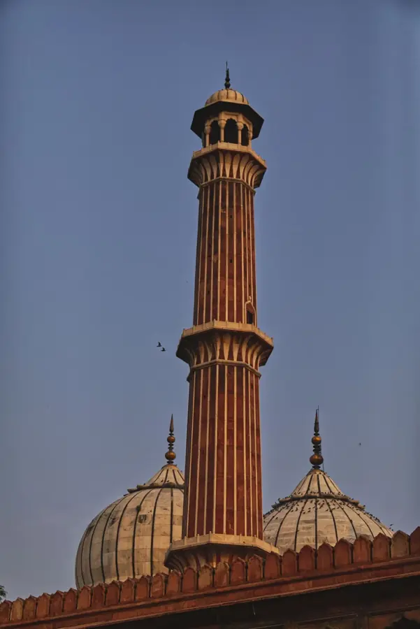Un minareto di arenaria rossa e due cupole di marmo della Jama Masjid, nel cielo della sera