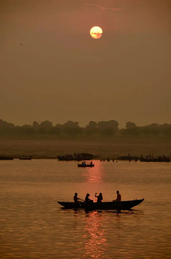 Una barca in controluce sul Gange mentre il sole sorge nella foschia, a Varanasi