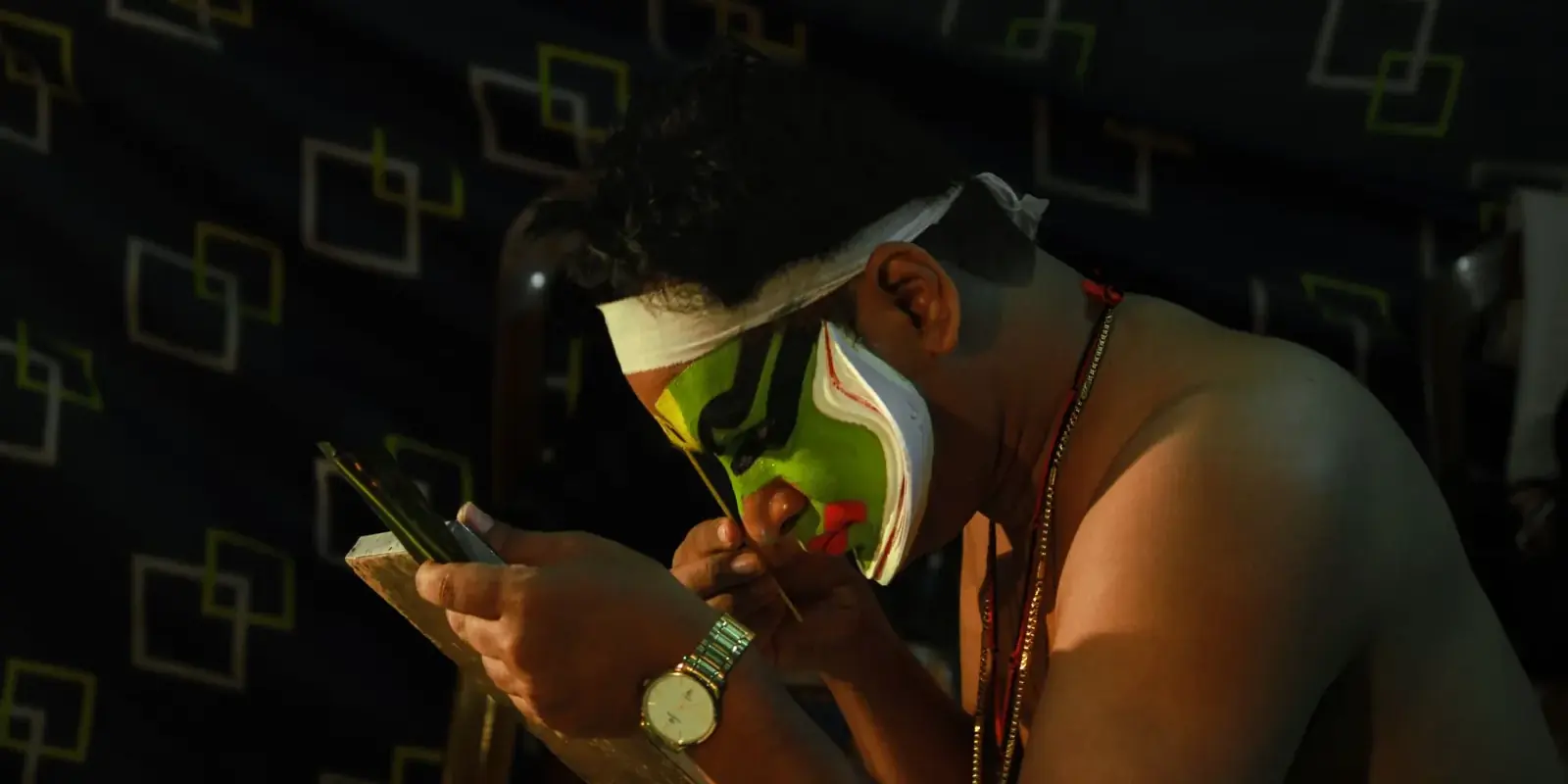 Attore di Kathakali che si dipinge il volto di verde allo specchio prima dello spettacolo