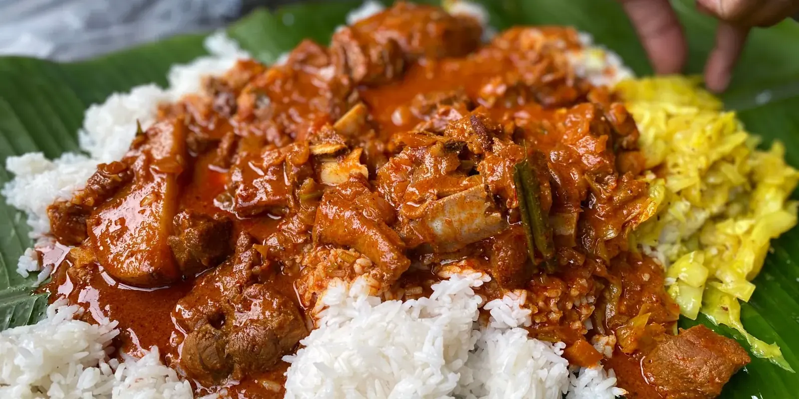 Riso bianco e curry serviti su una foglia di banano, una mano che si avvicina al piatto