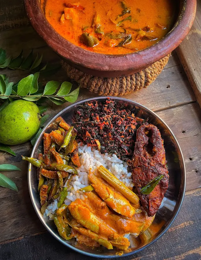 Curry di pesce in una pentola di terracotta e un piatto di riso, pesce fritto e verdure su un tavolo di legno