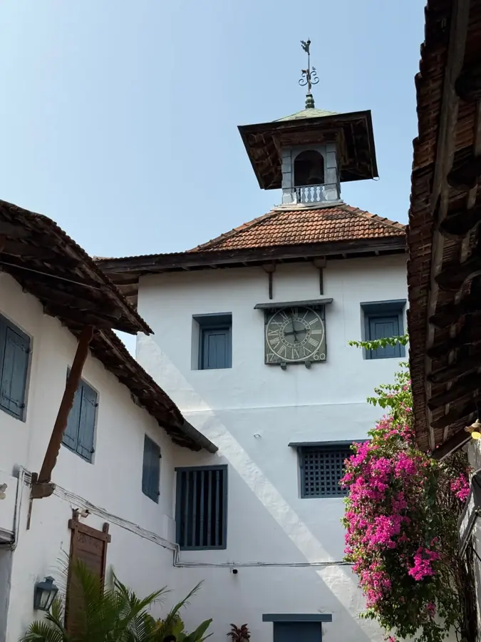 La torre dell'orologio della sinagoga Paradesi tra muri bianchi e una bouganville fiorita