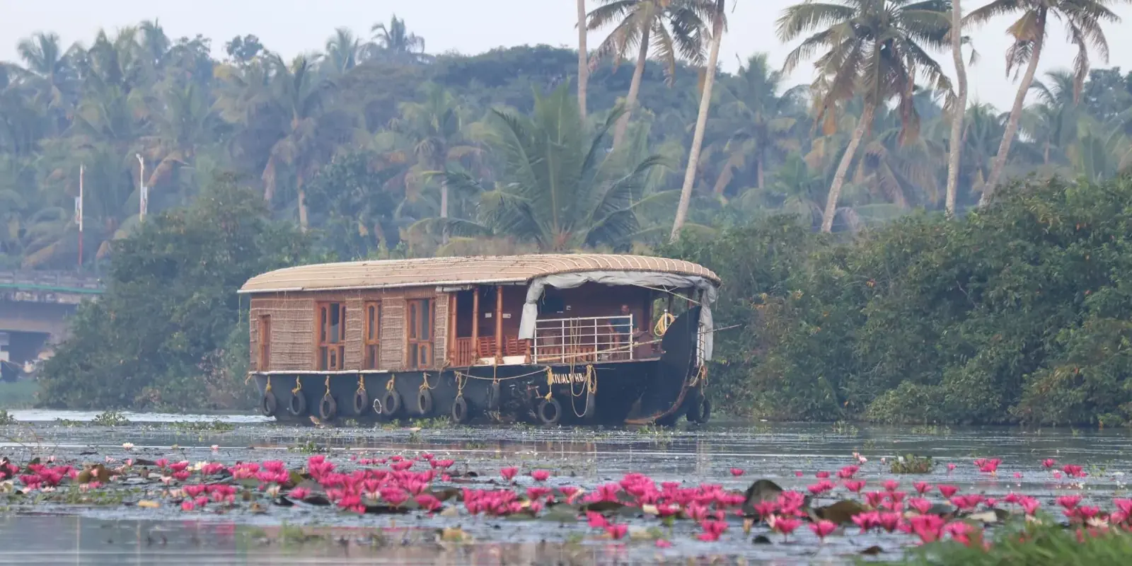 Kettuvallam con il tetto di paglia intrecciata che scivola sulle backwaters tra palme e ninfee rosa