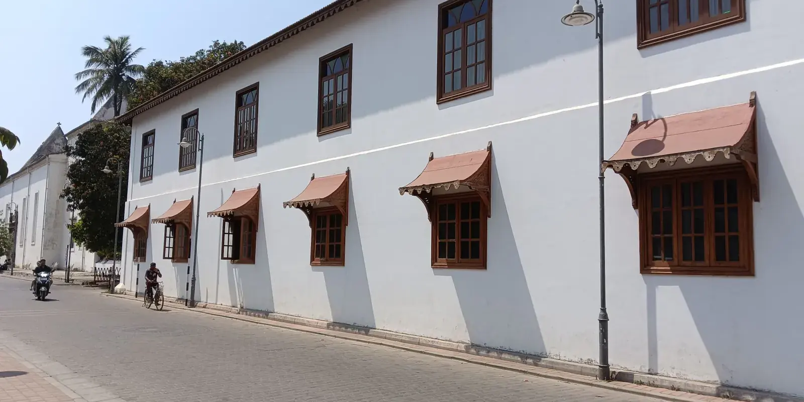 Edificio coloniale bianco con persiane di legno e tettoie rosse su una strada di Fort Kochi, un ciclista che passa