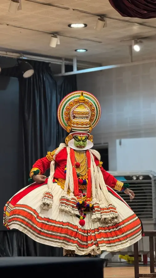 Danzatore di Kathakali in costume completo, gonna bianca e rossa e copricapo dorato, in una sala