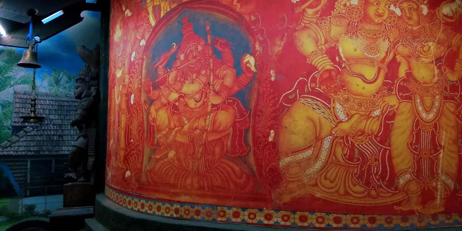 Grande pittura murale del Kerala su fondo rosso con divinità dai toni ocra e oro, in un museo