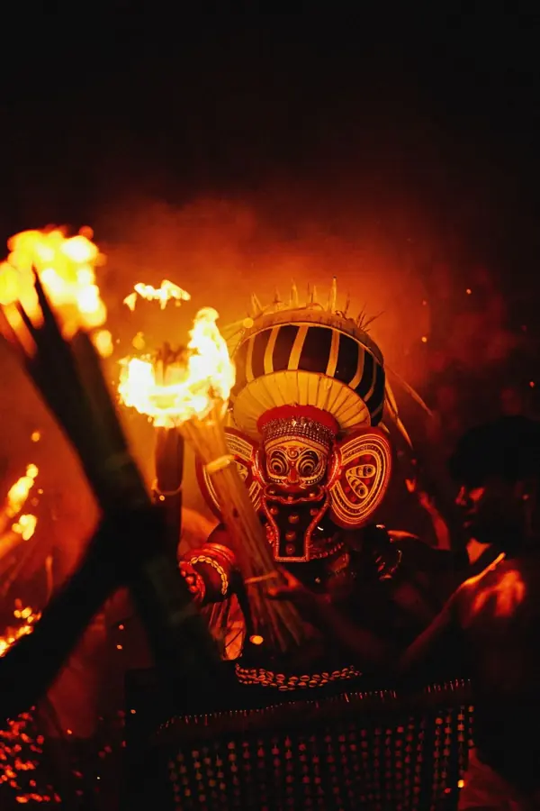 Theyyam di notte avvolto dalle fiamme delle torce, con il volto dipinto e il copricapo