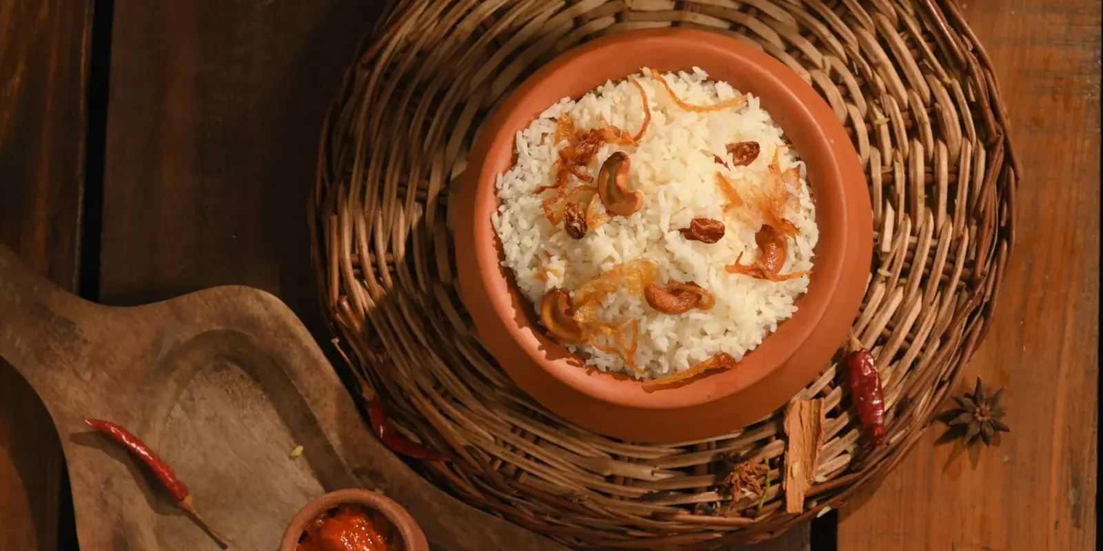 Riso del Kerala con anacardi e cipolle fritte in una ciotola di terracotta su un cesto, con salse e peperoncini