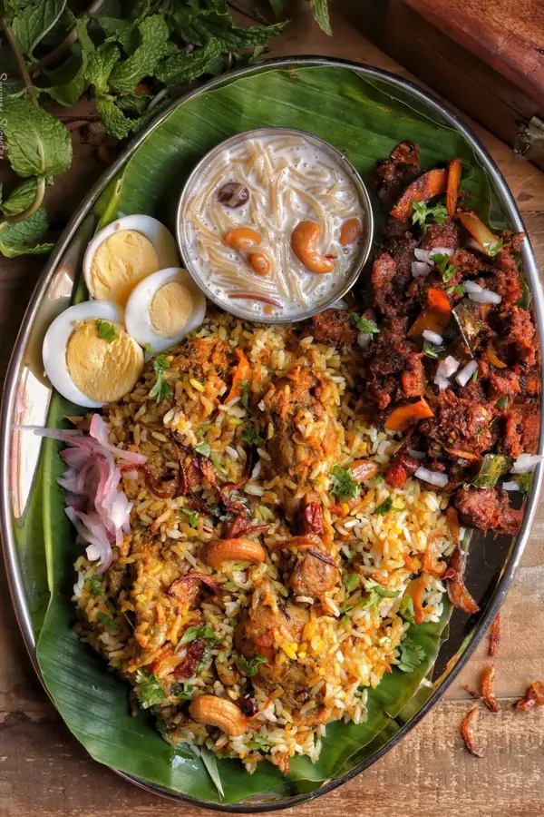 Biryani servito su foglia di banano con uova sode, carne fritta e una ciotola di payasam