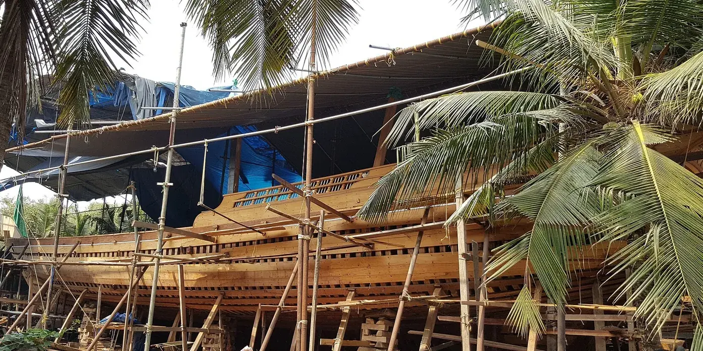 Grande uru di legno in costruzione tra impalcature e palme nel cantiere di Beypore