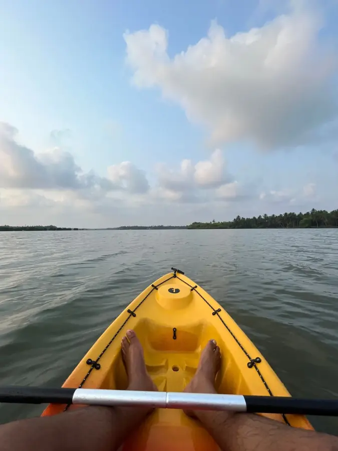 Prua di un kayak giallo e pagaia sull'ampia laguna di Thrikkaripur, con la riva verde all'orizzonte