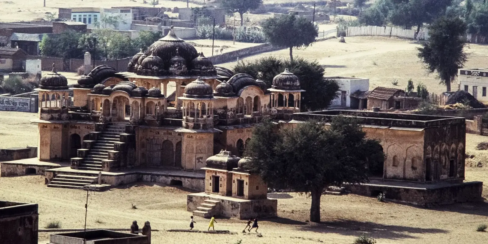Veduta dall'alto di un antico palazzo in pietra ocra con cupole e scalinate, in un villaggio rurale del Rajasthan