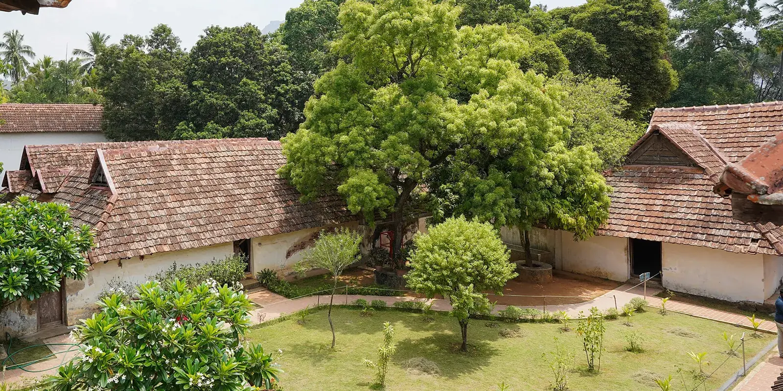 Il cortile verde di un palazzo tradizionale del Kerala con i tetti spioventi di tegole e le verande in legno