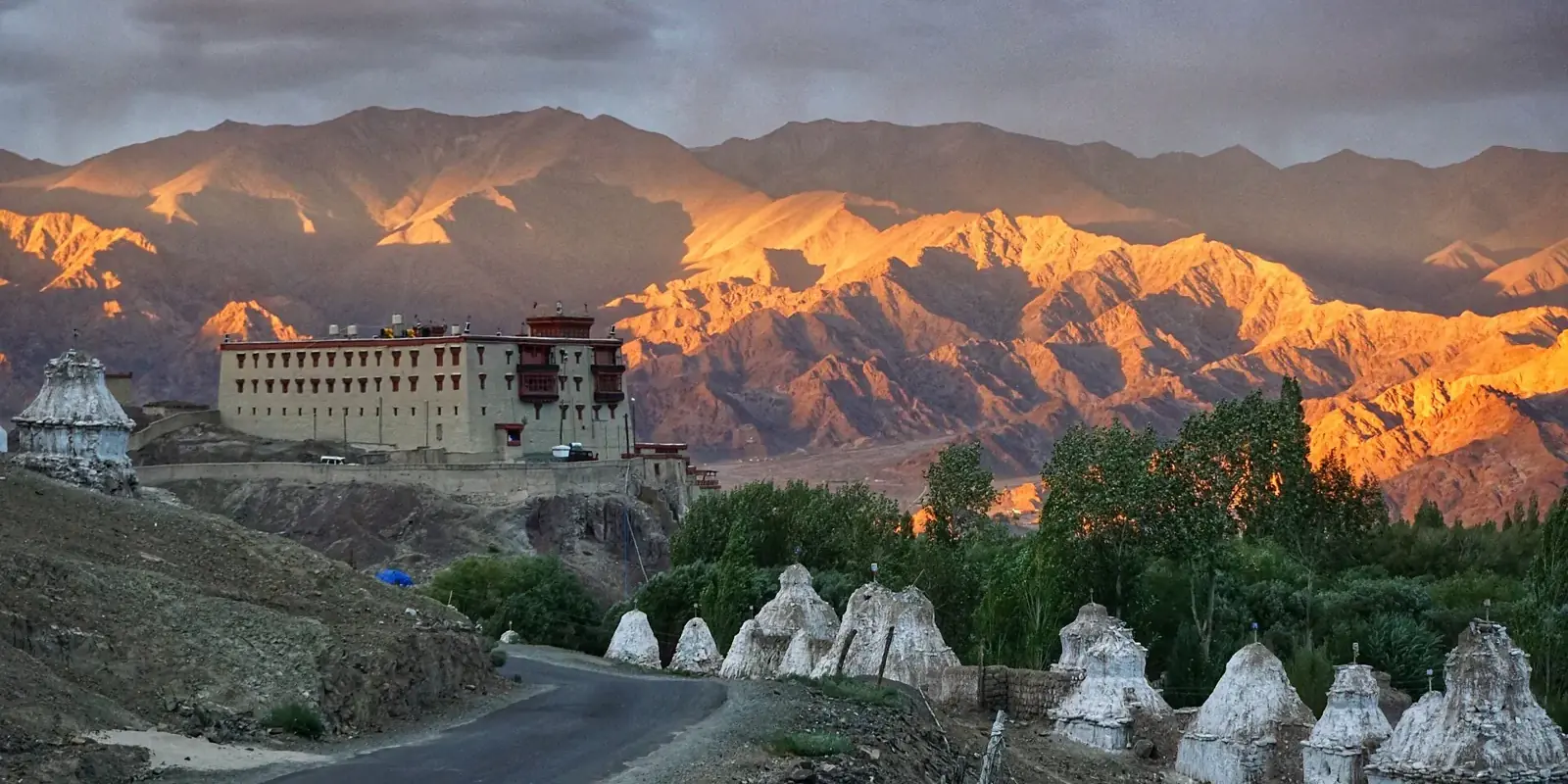 Lo Stok Palace imbiancato sul suo sperone di roccia, con i chorten bianchi in primo piano e le montagne del Ladakh accese dal sole