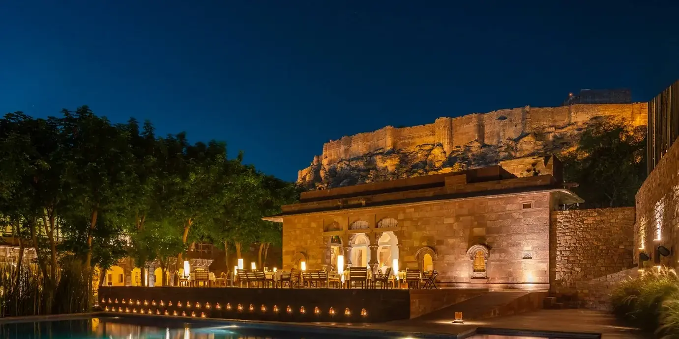 La piscina e il ristorante del RAAS Jodhpur di notte, con il forte di Mehrangarh illuminato sopra