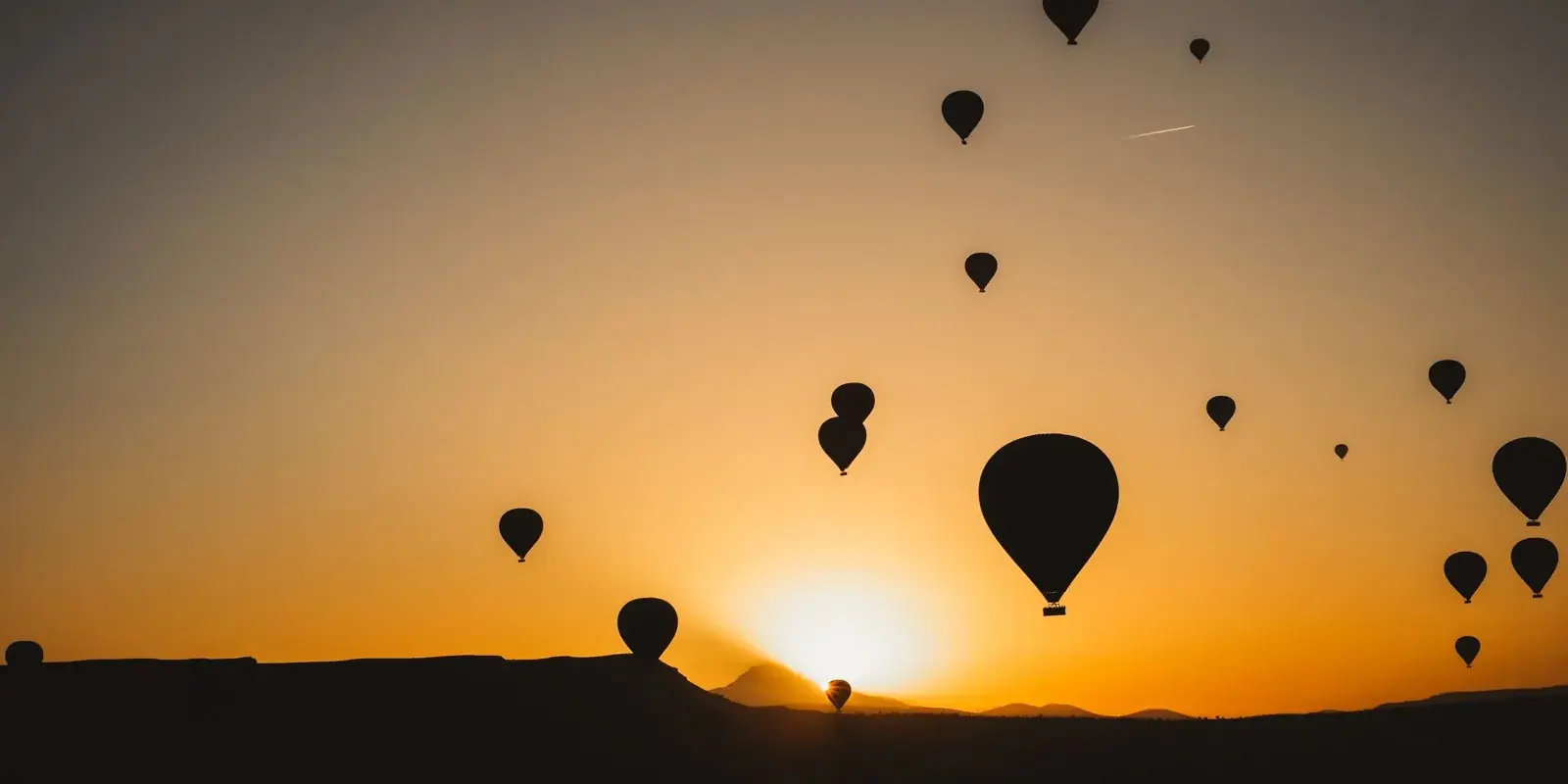 Sagome di mongolfiere nel cielo arancione, con il sole che spunta all’orizzonte