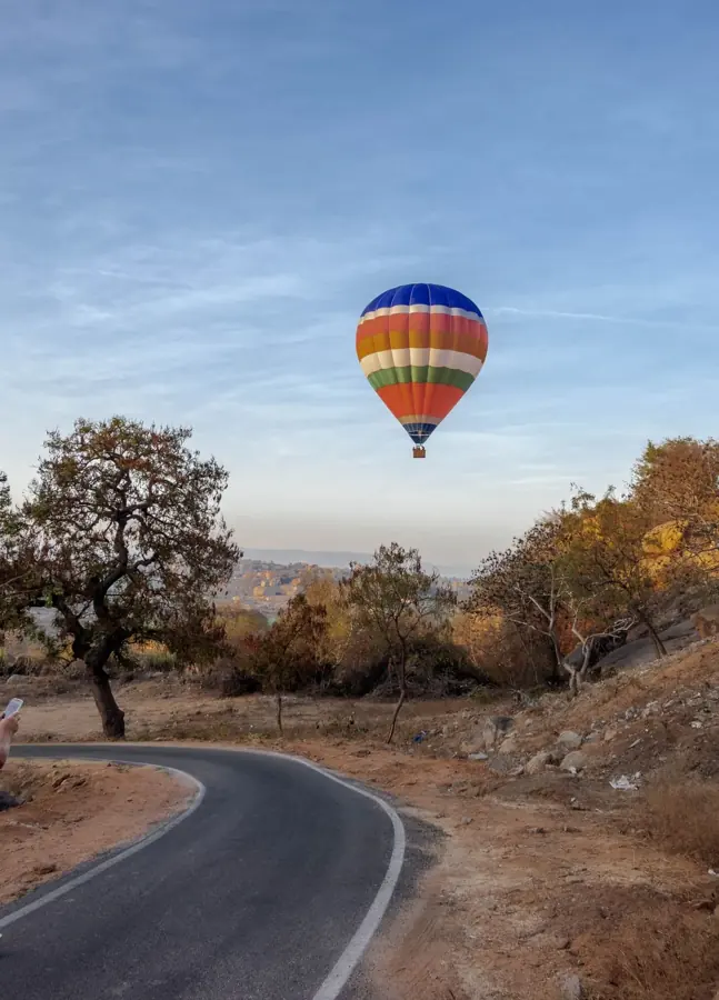 Una mongolfiera a strisce colorate sopra una strada di campagna indiana al mattino