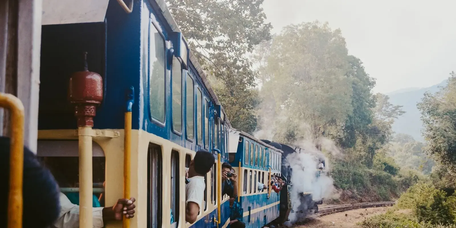 Il trenino blu e crema del Nilgiri, spinto dalla locomotiva a vapore, in curva tra le colline boscose