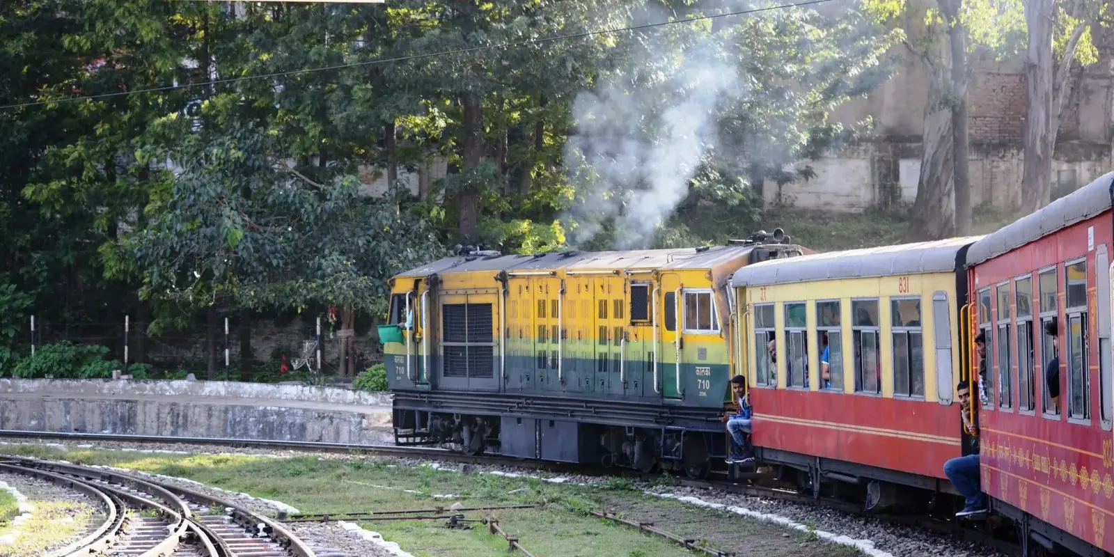 Il trenino della Kalka–Shimla con locomotiva gialla e verde e carrozze rosse in curva tra gli alberi