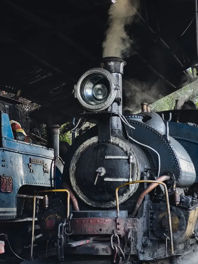 Frontale di una locomotiva a vapore del toy train di Darjeeling, con il grande fanale e il fumo, nel deposito