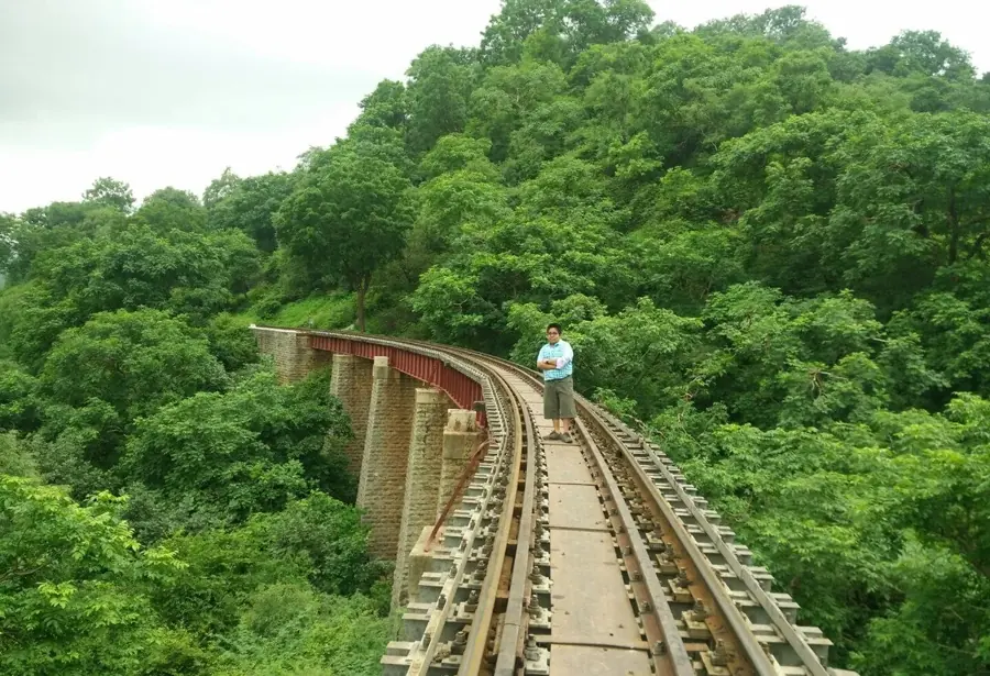 Il ponte ferroviario in curva di Goram Ghat sopra la gola coperta di boschi, con un visitatore sui binari
